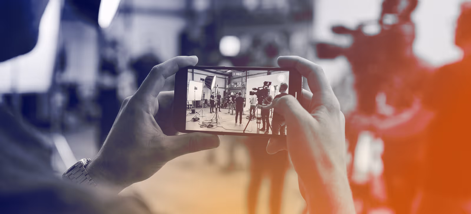 Person holding phone filming a video shoot with cameras and lights in a studio.