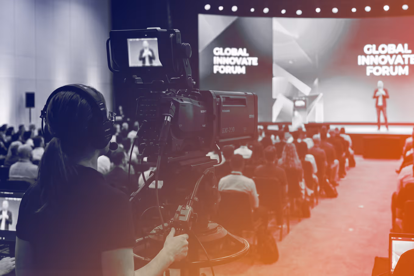 Camera operator filming a speaker onstage at the Global Innovate Forum with an audience seated.