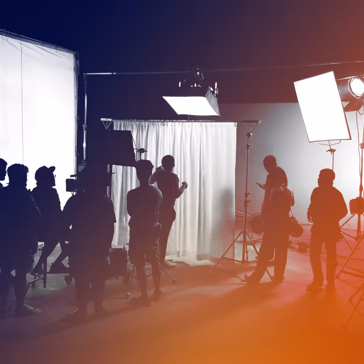 Silhouettes of crew members setting up lighting and camera equipment on a film set behind white curtains.