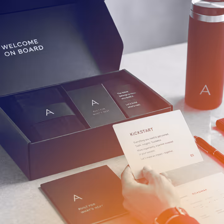 Open black welcome box with branded items and a person holding a card titled Kickstart.