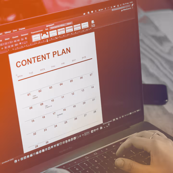 Person working on digital content plan calendar on a laptop keyboard with hand visible.