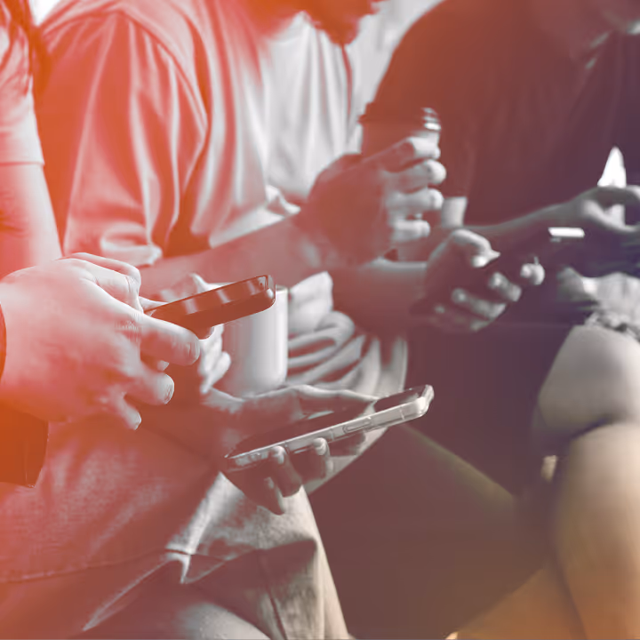 Close-up of several people sitting and using smartphones with a warm red light overlay.