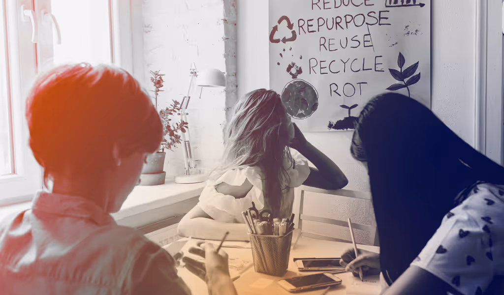 Three children sitting at a table working on art with a poster on the wall showing eco-friendly words.