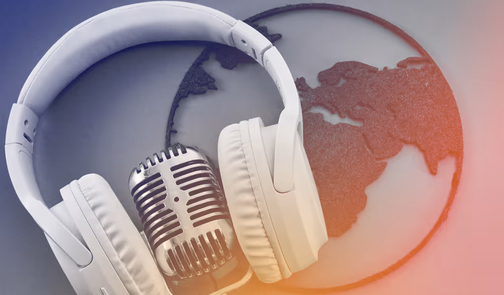 White headphones resting on a vintage microphone in front of a globe showing continents.