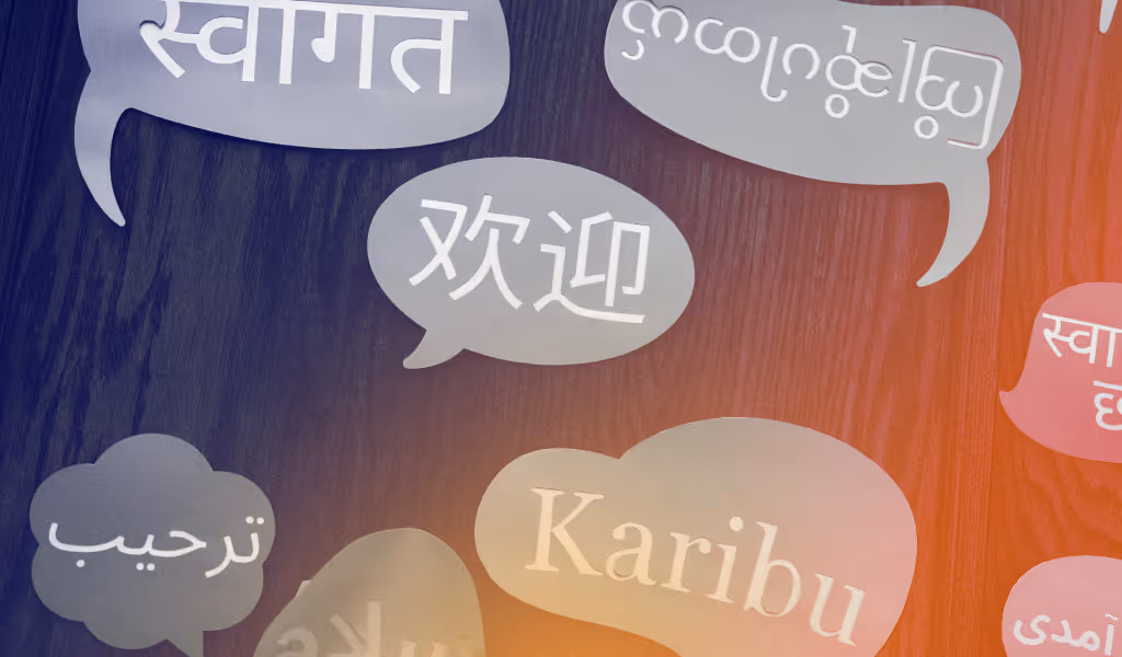 Speech bubbles with the word 'Welcome' in multiple languages on a wooden background.