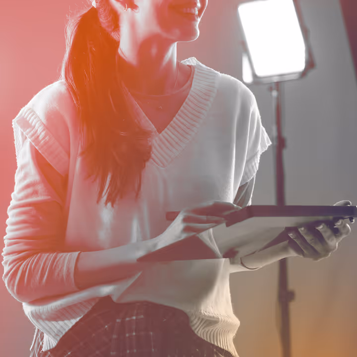 Smiling woman holding a tablet and stylus with studio light in the background.