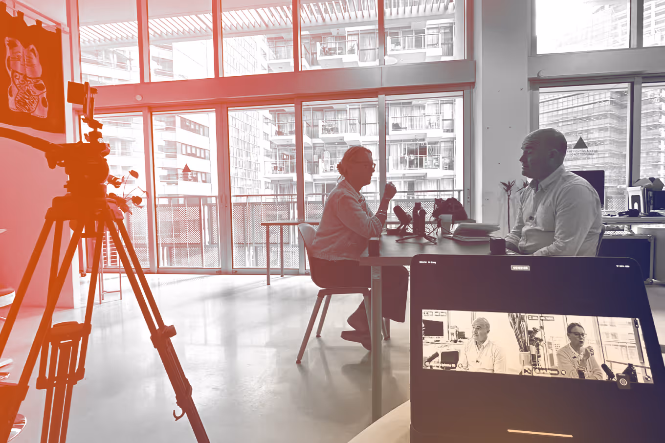 Two people having an interview in a bright room recorded by a camera and shown on a tablet screen.