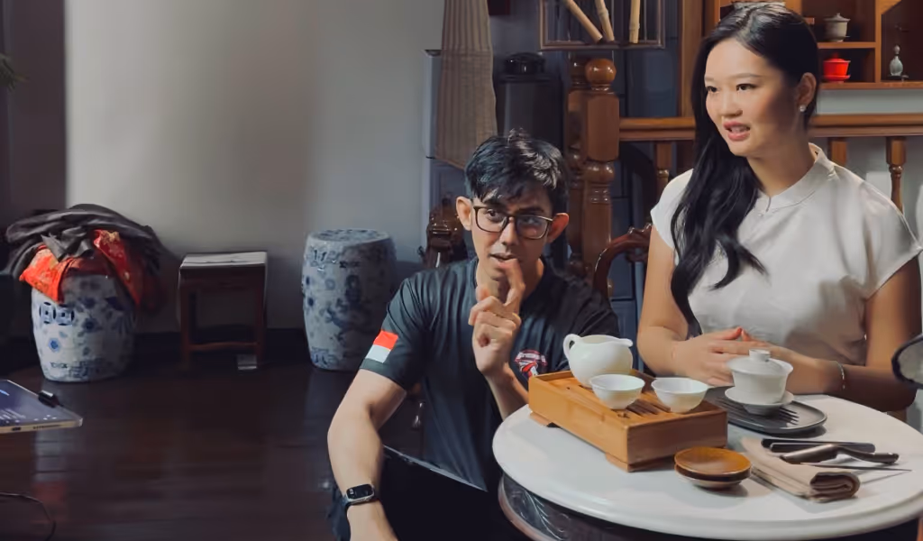 Man and woman sitting near a table with a tea set engaged in conversation indoors.