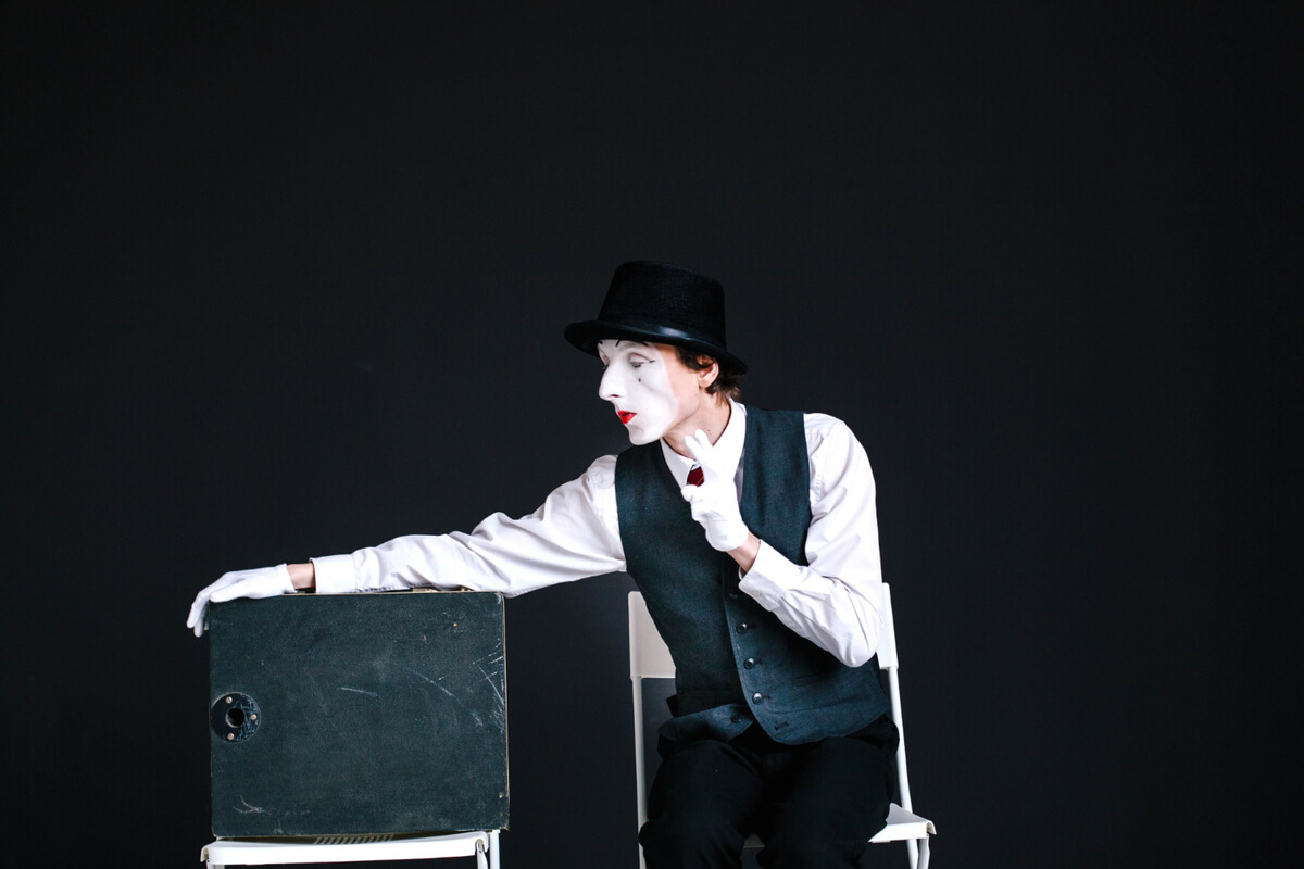 Illustrasjon av en pantomimeutøver som sitter på en stol og gestikulerer med hvitmalt ansikt og hatt, brukt som illustrasjonsbilde for beskrivelsen av familieforestillinger og teater for barn på Sandnes kulturhus