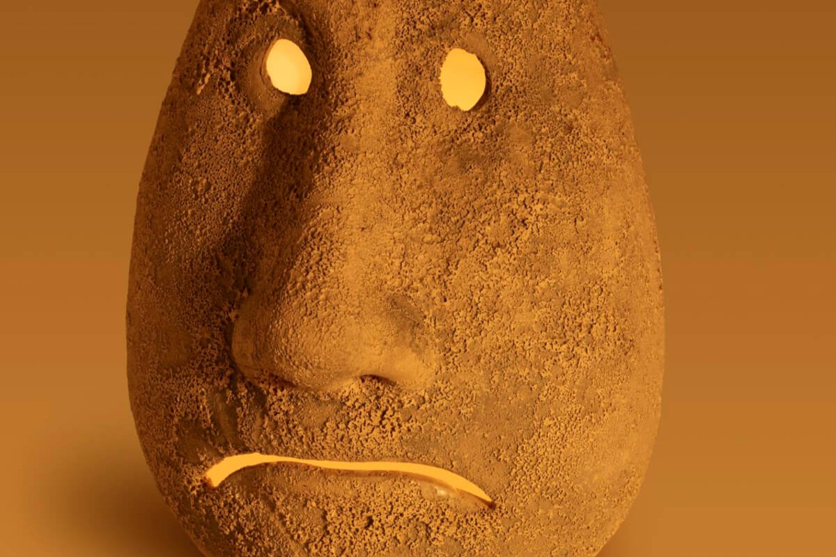 Et kunstverk formet som et ansikt laget av jord eller leire, med en nøytral brun bakgrunn