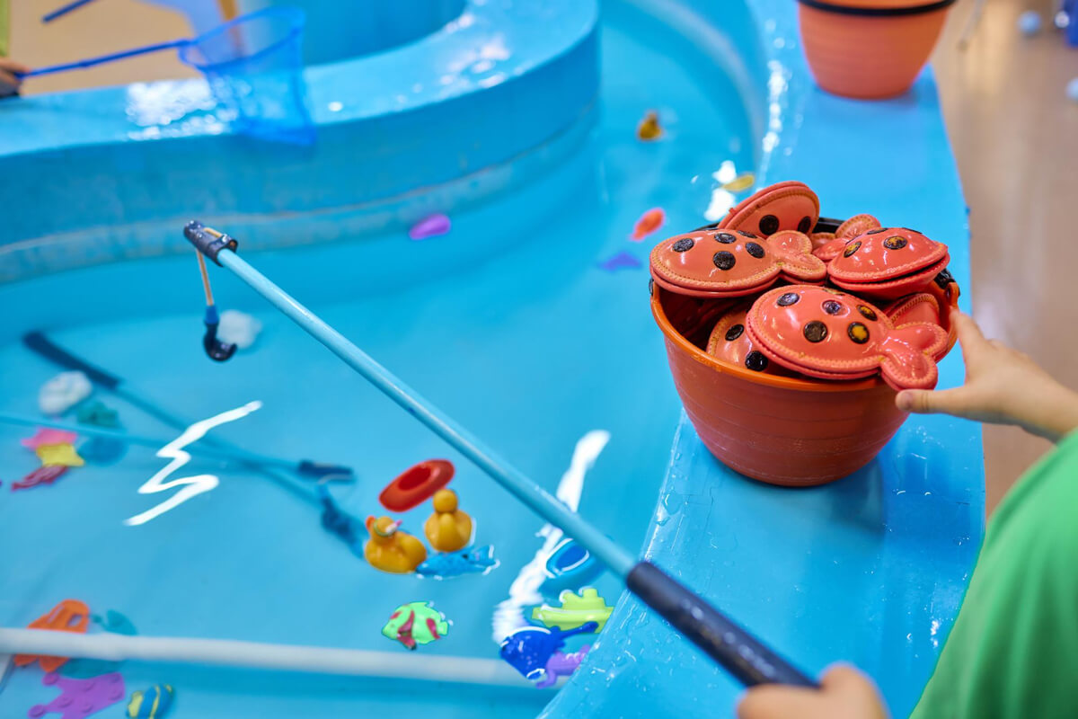 Et barn fisker opp små plastleker fra et blått basseng med fiskestang under et lekespill