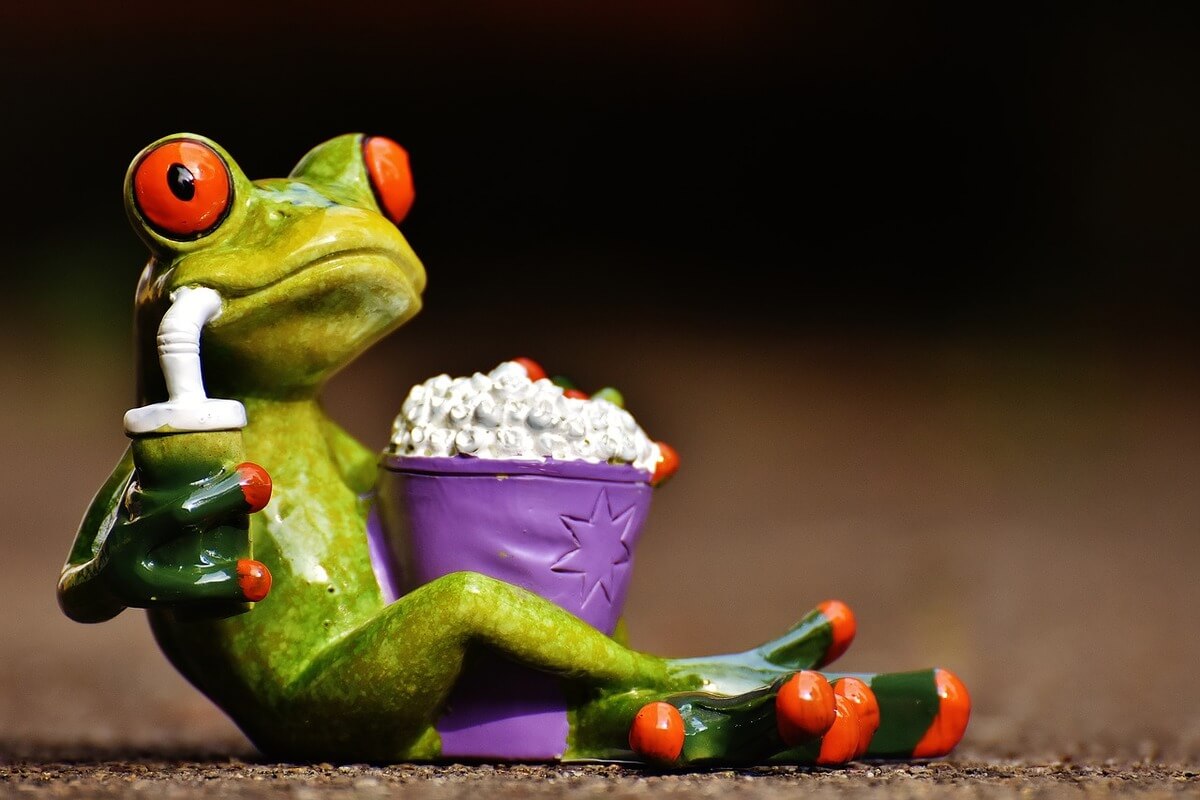 Grønn keramikkfrosk med beger med popcorn og krus med sugerør som illustrasjonsbilde for fredagsfilm på Deichman Bjørnholt