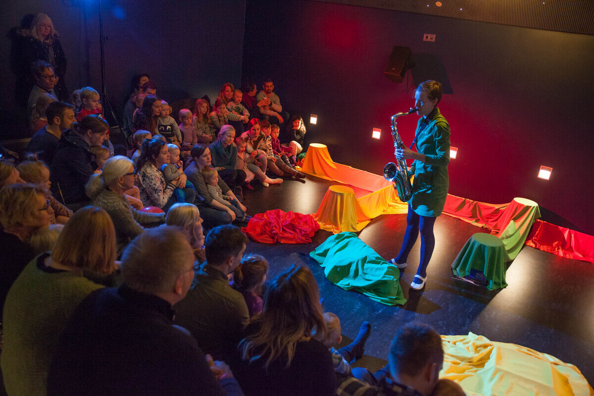 En musiker spiller saksofon foran et publikum av små barn og foreldre under den sanselige barneforestillingen «Kling Klang» på Sentralen i Oslo