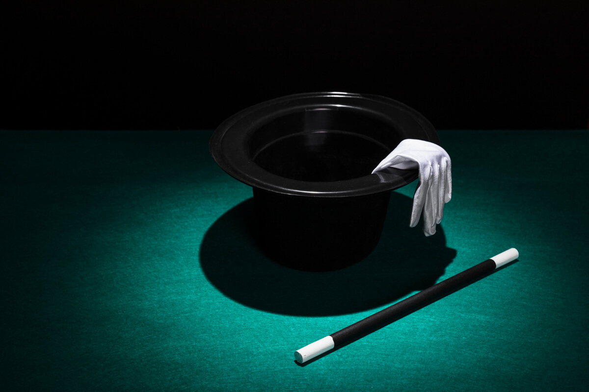 En tryllehatt med hvit hanske på kanten og en tryllestav liggende foran på grønt bord