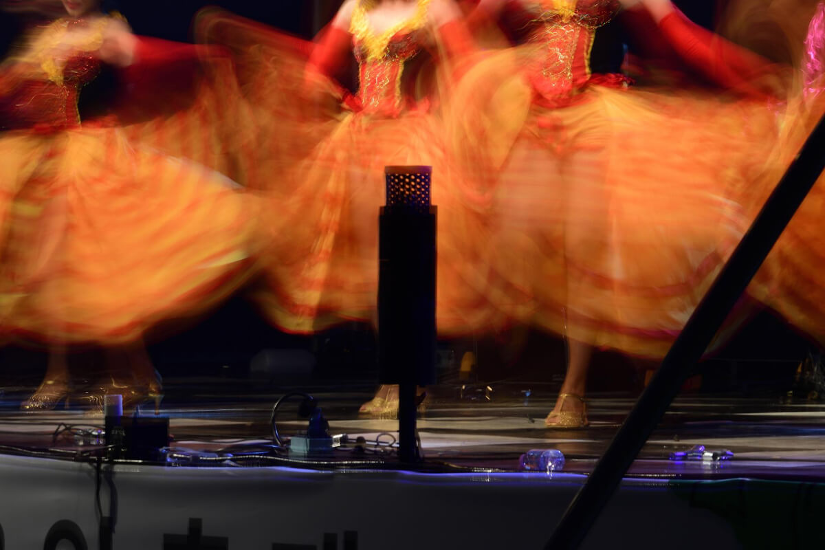 Uskarpt bilde av dansere i fargerike, røde og gule kjoler som snurrer på scenen som illustrasjon til beskrivelsen av Familieforestillinger og teater for barn i Stormen Konserthus