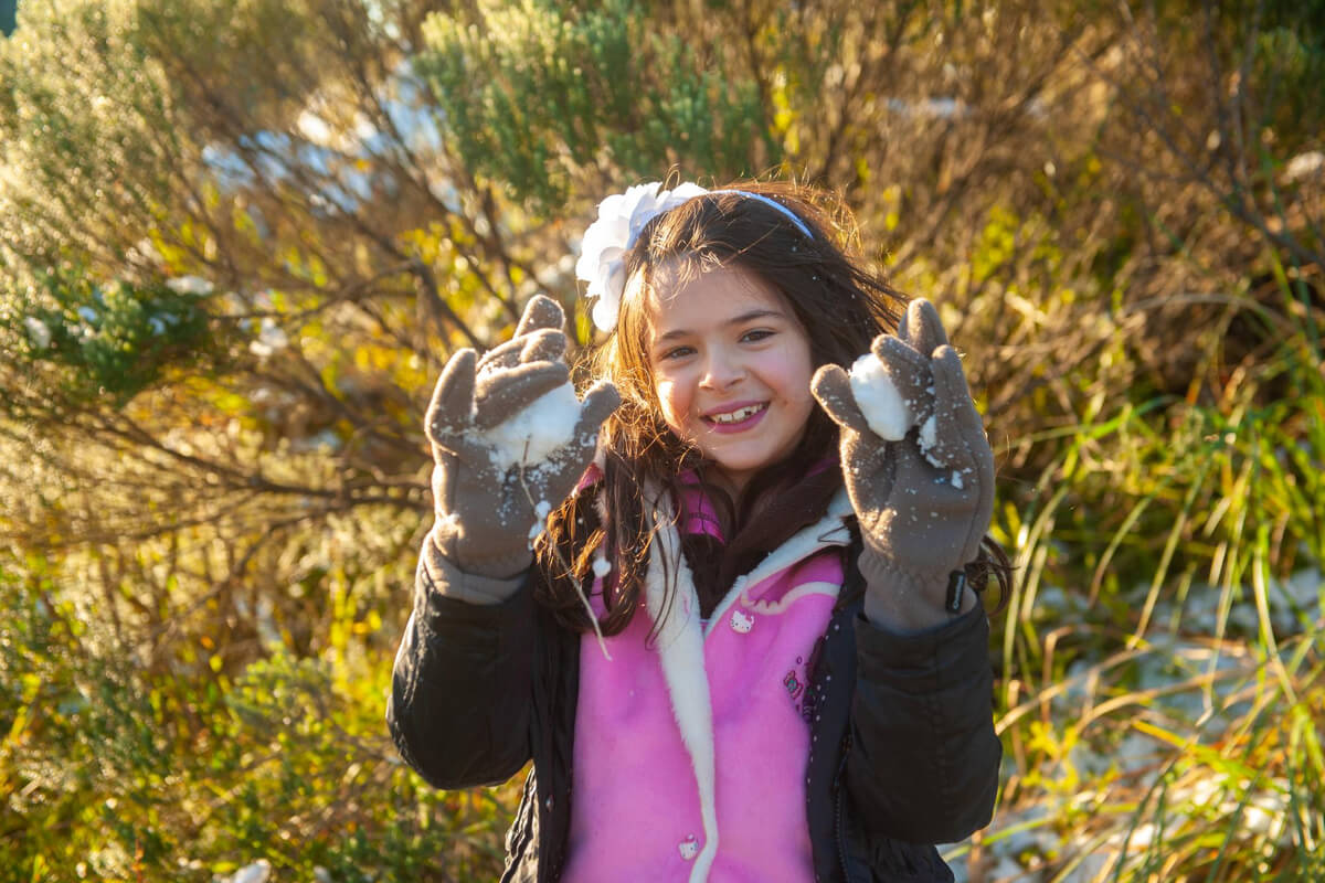 Smilende jente med mørkt hår og pink vest med en snøball i hver hånd som illustrasjon for Kom deg ut-dagen i Sandnes