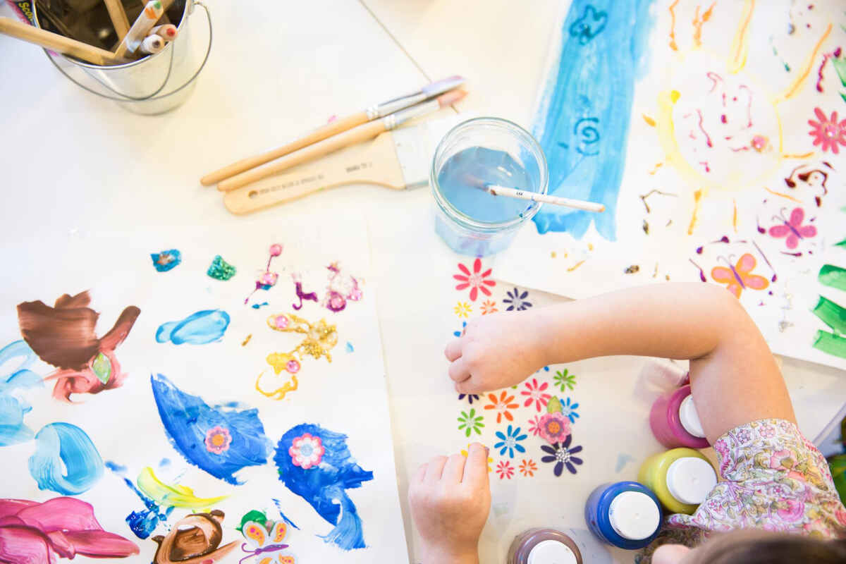 Et barn maler og lager kunst med farger, pensler og papir på et kreativt verksted