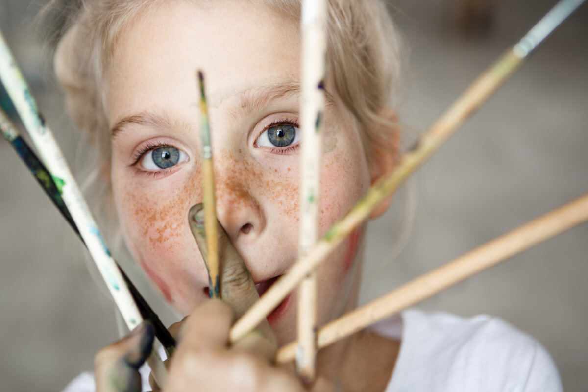 Nærbilde av jente som holder flere malerpensler foran ansiktet som illustrasjonsbilde til vinterferieverksted på MUNCH