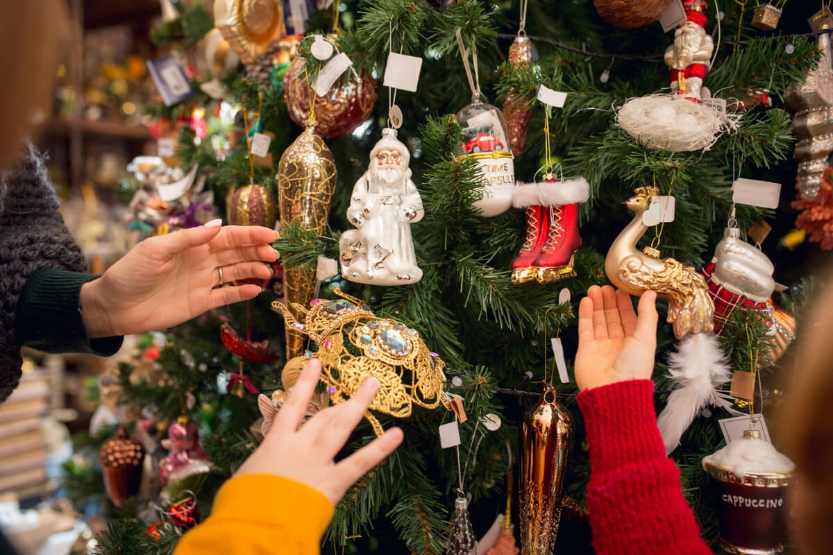 Nærbilde av juletre med mye pynt og tre hender som tar på hver sin pynt som illustrasjon til Jul på Karljohansvern