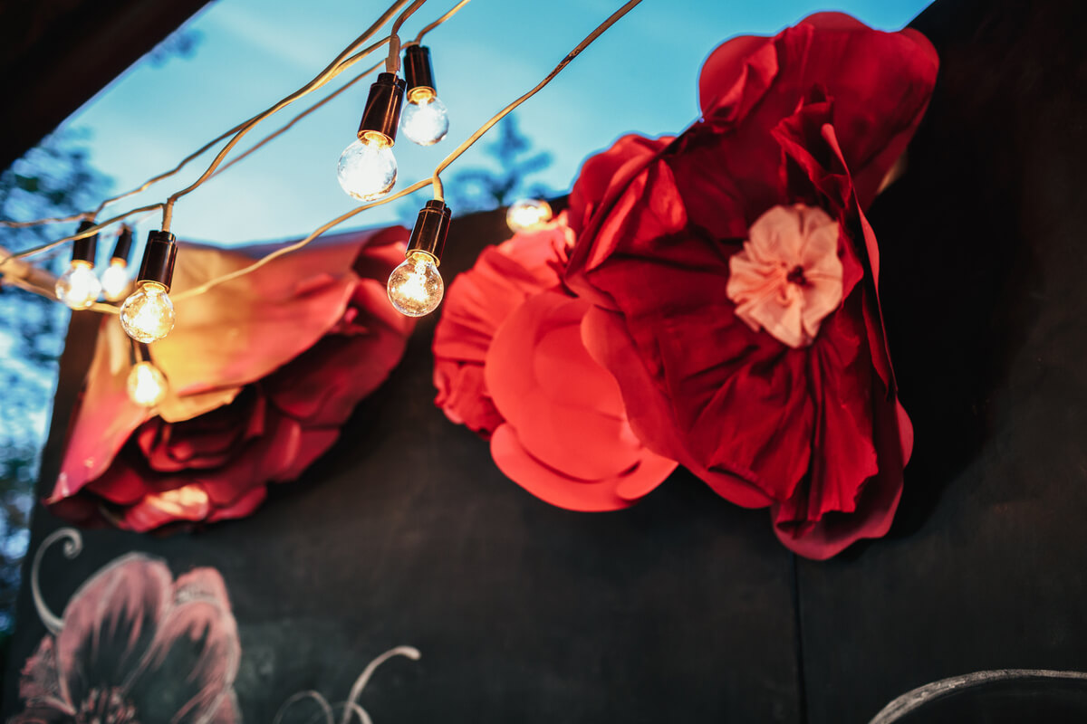 Dekorative teaterrekvisitter med store røde papirblomster og lyslenke, fotografert utendørs i forbindelse med en scenisk forestilling eller kulturarrangement