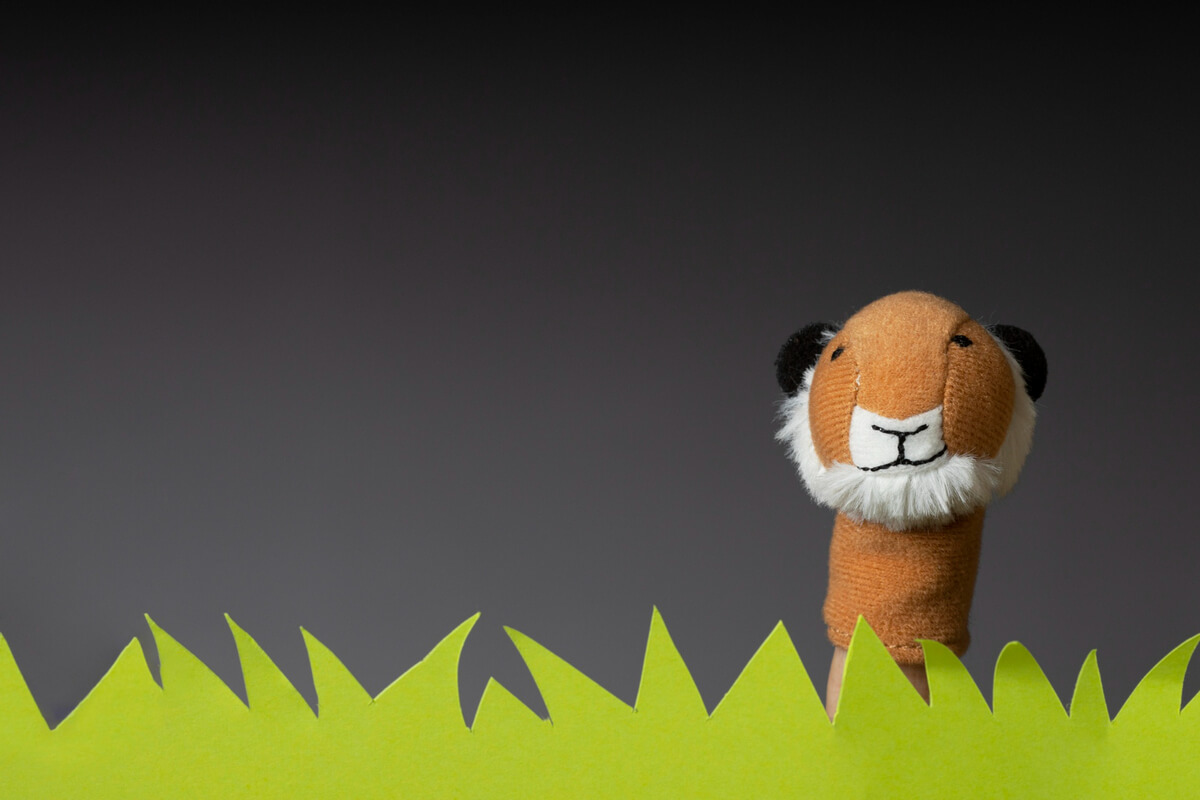 En tigerfingerdukke stikker opp bak grønne papptagger som forestiller gress, som illustrasjonsbilde for beskrivelsen av Familielørdag på Ny-Krohnborg fellesbibliotek