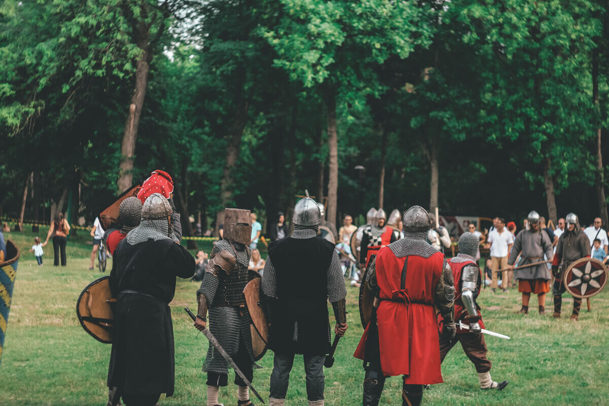 Vikinger i autentiske kostymer deltar i kampshow under en vikingfestival. Publikum ser på mens deltakerne i rustninger og med skjold og sverd gjør seg klare til kamp i grønne omgivelser