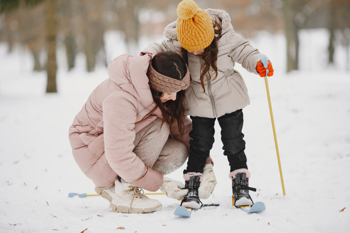 Mor som hjelper datteren på med skiene som illustrasjonsbilde for vinterferieaktiviteter på skileikområdet ved Vestli / Stovner
