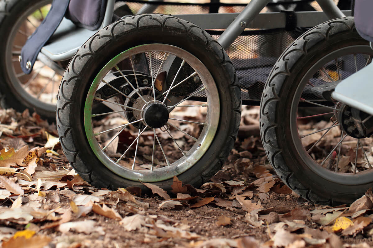 Nærbilde av barnevognhjul med eiker på sti dekket av tørre høstblader