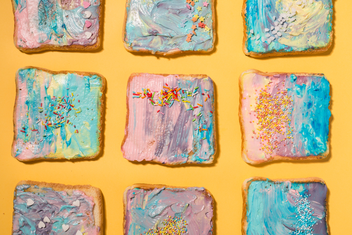 Fargerike brødskiver med smørkrem og strøssel ligger i et rutemønster på gul bakgrunn som illustrasjonsbilde for beskrivelsen av Babyomvisning på Kunstnernes Hus