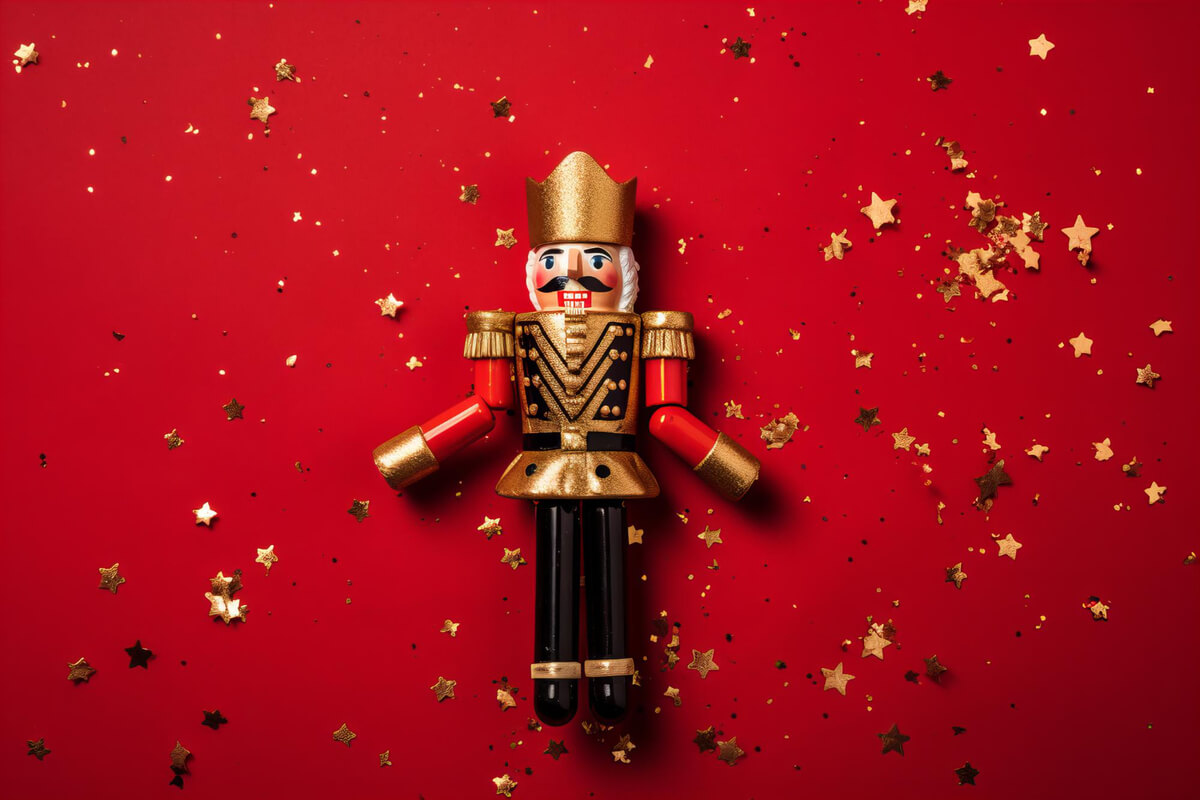 En klassisk nøtteknekkerfigur med gull og røde detaljer ligger på rød bakgrunn pyntet med gullstjerner som illustrasjonsbilde for familieforestillingen Nøtteknekkeren med Teaterlaget BUL Nidaros