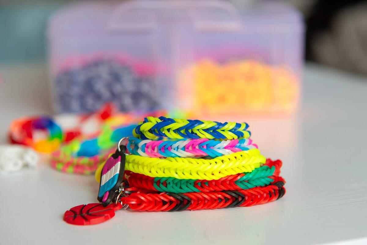 Armbånd av stoff i sterke farger og en plastboks med innhold i bakgrunnen som illustrasjonsbilde til beskrivelsen av vinterferieaktiviteter på Deichman Tøyen