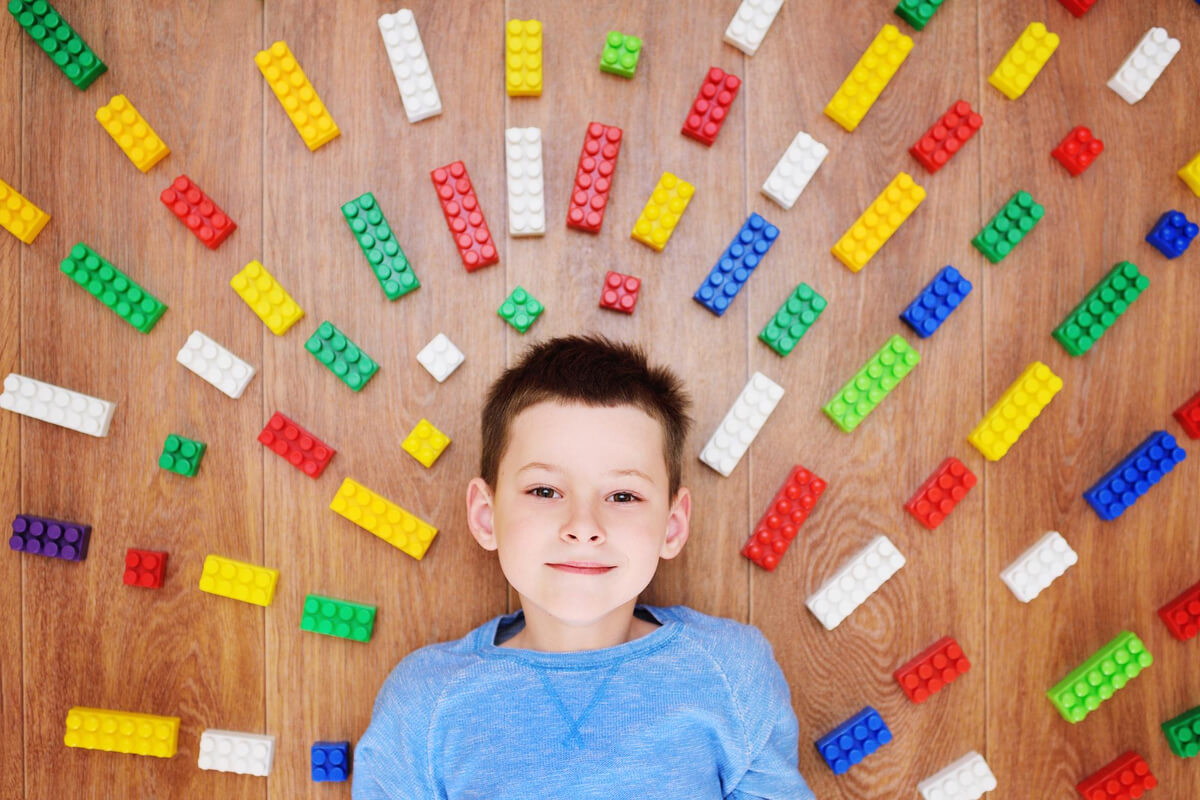 Gutt som ligger på LEGO-klosser plassert i bue rundt hodet som hans som illustrasjonsbilde for vinterferieverksteder på Bekkestua bibliotek
