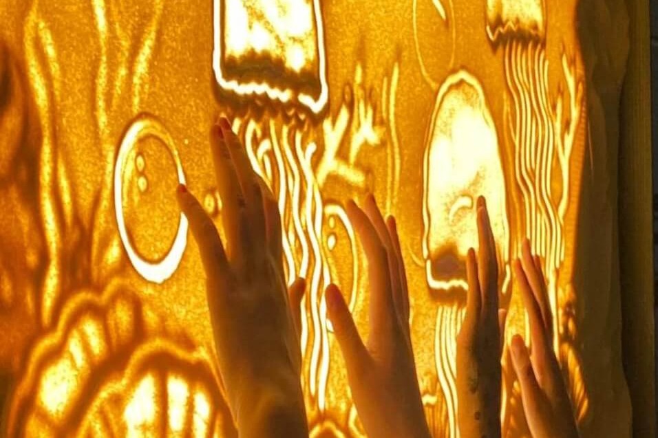 Hender som lager i figurer i sand på en gjennomlyst plate som illustrasjon for workshop med Lysteater på Sentralen