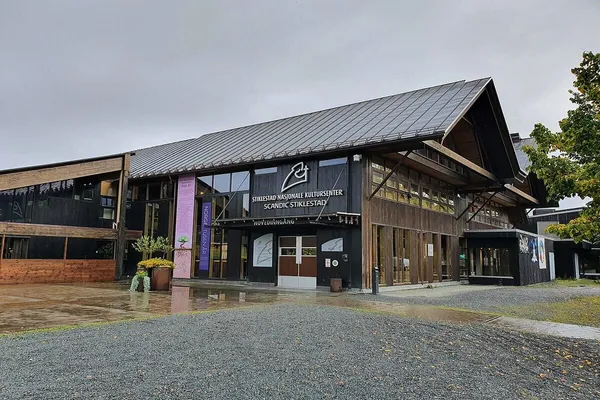 Inngangspartiet til Kulturhuset på Stiklestad Nasjonale Kultursenter, brunt trehus med saltak og diverse skilt rundt inngangen