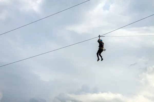 Person i zip-line i silhuett mot en overskyet himmel