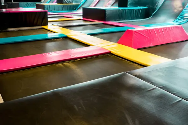 Svarte trampolinematter med fargerike plastmatter mellom som illustrasjonsbilde for beskrivelsen av FlipZone trampolinepark i Bergen