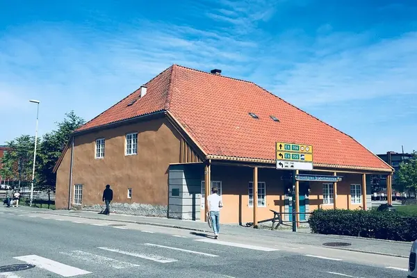En terracottafarget bygning i stein med røde tegl på taket som romme Trondhjems Sjøfartsmuseum, beliggende helt inntil en vei 