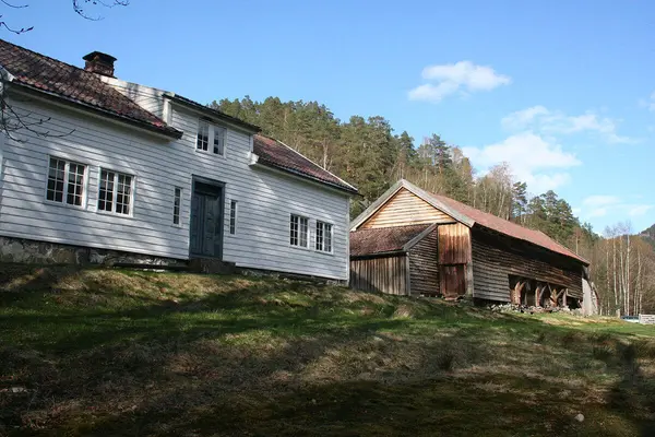 Stuehuset og låven på Kolbeinstveit museumsgård sett skrått nedenfra tunet med blå himmel i bakgrunnen