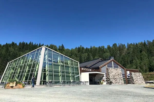 Moderne museumsbygg med glassfasade og uteservering, omgitt av skogkledd landskap ved Vest-Telemark Museum Eidsborg