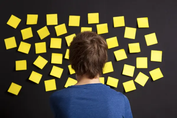 En person ser på en vegg dekket med mange gule post-it-lapper