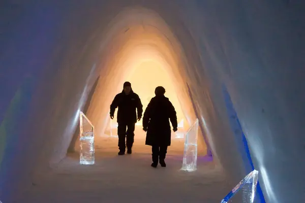 To personer som går gjennom en buet korridor laget av is i Krikenes snøhotell