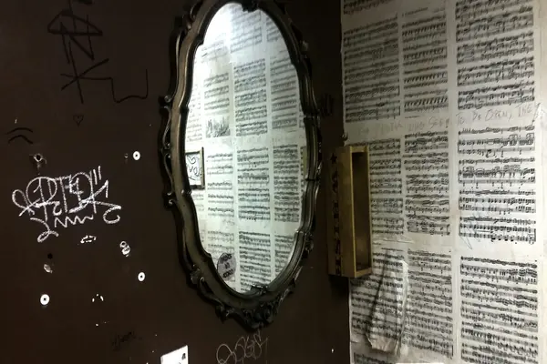 Et gammelt speil på en vegg dekket av noter og graffiti i et stemningsfullt rom