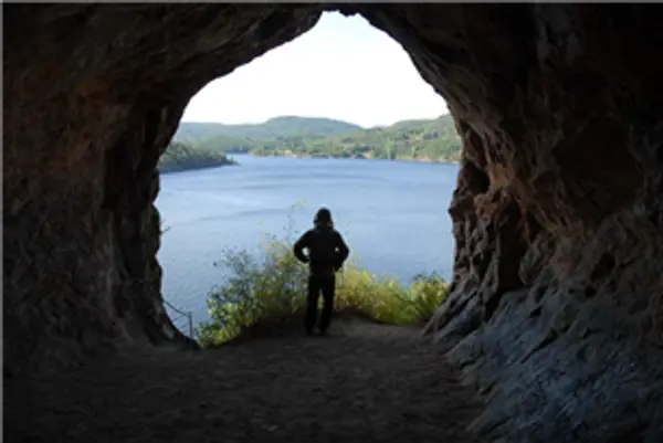 Hule fotografert innenfra med vann i bakgrunnen og en person i silhuett i åpningen