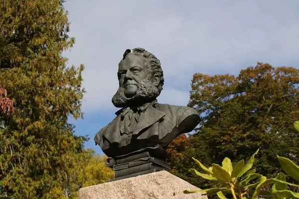 Statue i metall av Henrik Ibsen fra brystet og opp, stående på en firkantet pidestall av stein 