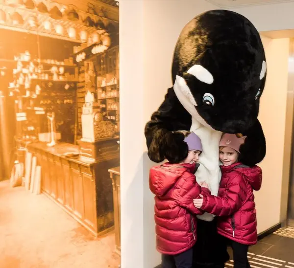  To barn som klemmer en person forkledd som hval på Hvalfangstmuseet