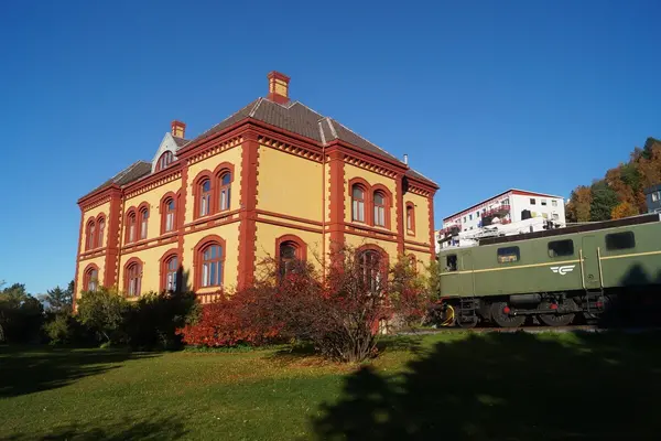 Gul museumsbygning med røde vinduskarmer og en grønn togvogn på utsiden 