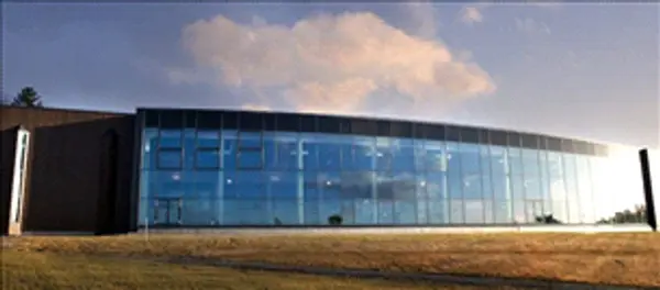  Glassfasade på oval bygningsfront med gressbakke foran og himmel over