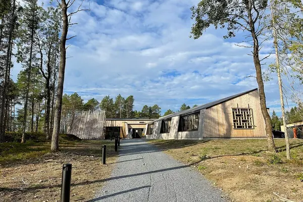 Innkjørselen til Saemien Sijte, en gruslagt gang- og kjørevei som slutter på en gårdsplass foran inngangen til museet, et moderne lavt trebygg med skrått tak og vegger og stor innbygde vinduer