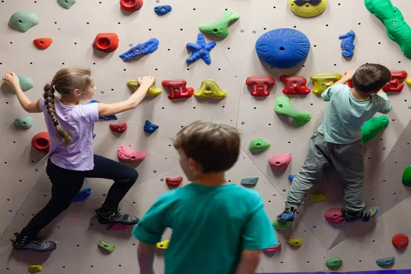 Tre barn i en buldrevegg med mange fargede gripehåndtak i Klatreverket Drammen på Strømsø