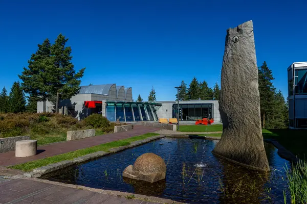 Galleri Würth i Nittedal omgitt av furutrær, med skulpturer og et vannbasseng i forgrunnen under en klar blå himmel